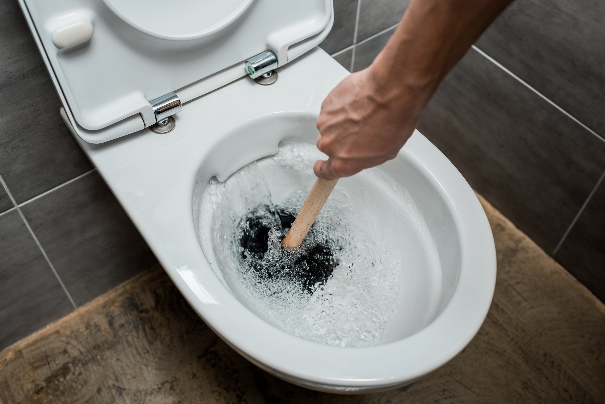 cropped view of plumber using plunger in toilet bowl during flushing in modern restroom with grey